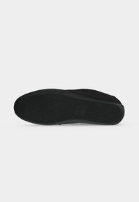 Semelle de chaussure noire avec un motif triangulaire texturé et une petite section rectangulaire avec un marquage discret au centre.