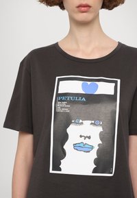 Donkergrijze katoenen t-shirt met een grafische print van een gestileerd gezicht met blauwe accenten, omlijst door een witte rand en tekst eronder.