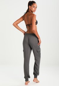 Schwarzer Bikini-Oberteil und graue Cargo-Jogginghosen mit Seitentaschen, elastischen Bündchen und lockerer Passform, die eine glatte Textur und ein leichtes Design präsentieren.