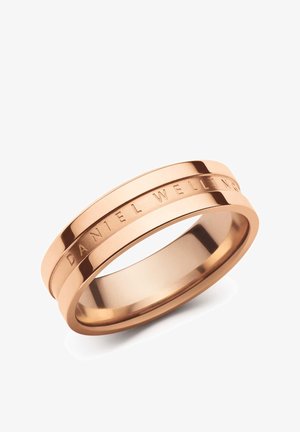 Bague en métal rose doré avec une rainure autour de l’anneau et un texte gravé « "DANIEL WELLINGTON" » sur la surface extérieure.