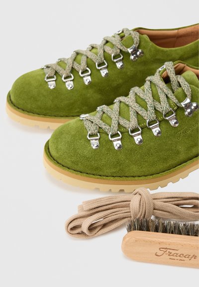 Vihreät mokkasiinisaappaat, joissa on hopeiset yksityiskohdat, khaki-nauhat ja beige kumipohja. Mukana beige kengännauha ja puhdistusharja.