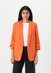 Orange blazer med skræddersyet pasform, notched klapper og trekvartærmer, parret med en hvid top og sorte bredbenede bukser.