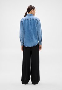 Džínová košeľa svetlomodrej farby s zadným dielom, dlhými rukávmi a manžetami na gombíky. Kombinovaná so širokými čiernymi nohavicami s hladkou textúrou látky.