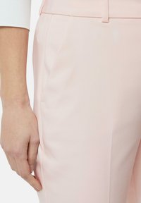 Pantaloni su misura di colore rosa chiaro con una texture liscia, tasche laterali e design frontale piatto. Sono visibili dettagli cuciti lungo le cuciture.