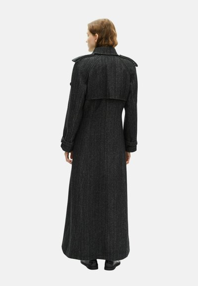 Lang zwart jasje van textuurstof, met een kraag in militaire stijl, schouderepauletten en een fitted silhouette met een uitlopende zoom.