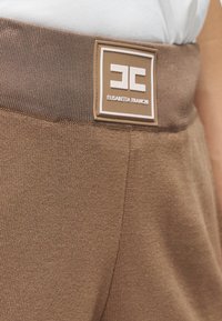 Καφέ πλεκτή μέση με ραμμένη ετικέτα που αναγράφει "Elisabetta Franchi." Η υφή φαίνεται ομαλή και ελαστική.