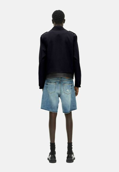 Giacca nera aderente con dettagli sulle spalle, abbinata a pantaloni corti in denim azzurro con orlo sfilacciato. Indossata con calze e scarpe nere.