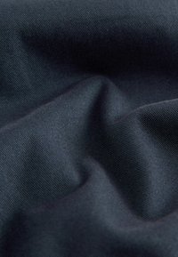 Dunkelmarineblaues Gewebe mit glatter Textur, das subtile gerippte Muster und sanfte Falten aufweist und das Licht sanft reflektiert.