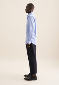 Lichtblauw en wit gestreepte overhemden met knoopmanchetten, gecombineerd met donkerblauwe broek en zwarte veterschoenen.