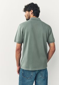 Skogsgrön pikétröja med kort krage, korta ärmar och sidospjäll, kombinerad med ljusblå denimjeans. Mjuk textur.