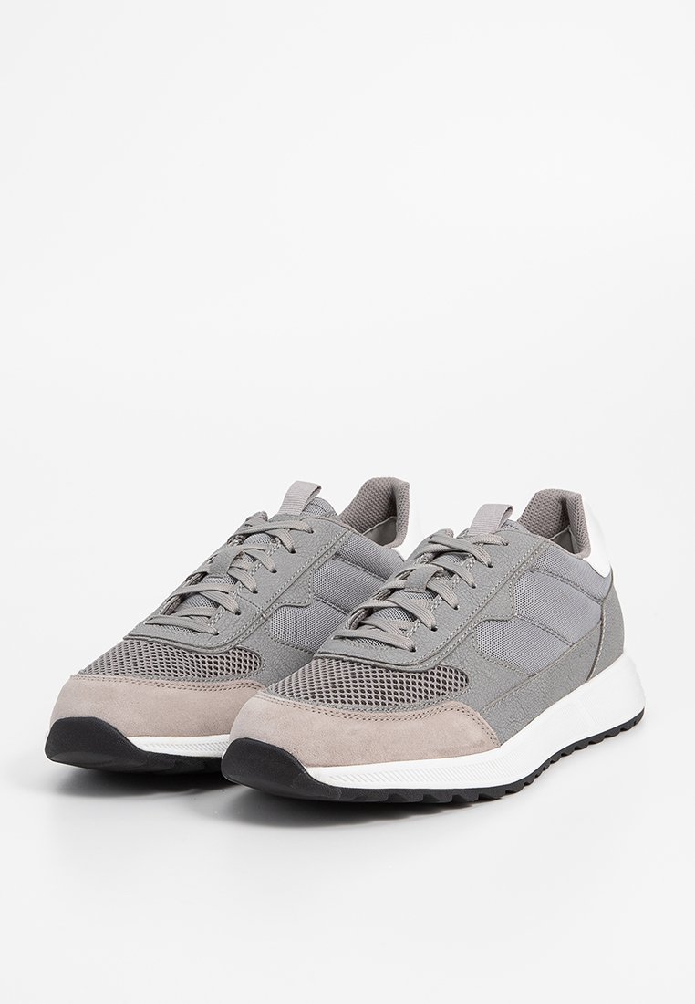 Graue Sportschuhe bestehen aus einer Kombination von Wildleder und Mesh-Materialien, mit einem strukturierten Obermaterial, Schnürsenkeln und einem weißen Mittelsohlenakzent.