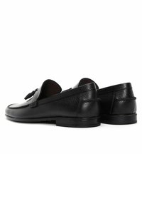 Black leather loafers with a textured finish, rounded toe, and low heel. Features decorative tassels and minimal stitching detail.