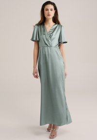 Satin maxi dress in light green with a V-neck, short flared sleeves, and a fitted waist. Features a side slit and flowing silhouette.