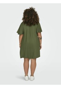 Alyvučių žalios spalvos suknelė su trumpomis plačiomis rankovėmis, iki kelių ilgio, pagaminta iš lengvos medžiagos ir laisvo silueto, derinama su baltais sportbačiais.