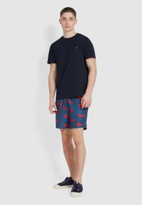 T-shirt di cotone blu navy abbinata a pantaloni corti blu con stampe di bassotto rossi. Sneakers blu navy con suole bianche. Design semplice e informale.