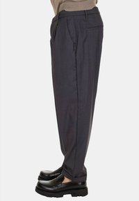 Pantaloni grigi su misura con vestibilità dritta, realizzati in tessuto leggero; presentano pieghe frontali e tasche laterali, abbinati a mocassini neri.