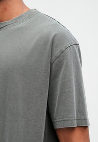 Sivá bavlnená tričko s krátkymi rukávmi, okrúhlym výstrihom a jemnou textúrou. Viditeľné švy pozdĺž goliera a rukávov. Pohodlný strih.