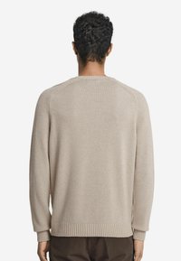 Beige Strickpullover mit geripptem Saum und Bündchen. Verfügt über Raglanärmel und einen klassischen Rundhalsausschnitt, der eine weiche Textur zeigt.