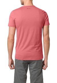 Červené tričko s krátkým rukávem vyrobené z jemné látky, s jednoduchým designem a malým logem poblíž výstřihu. Doplnené šedými šortkami.