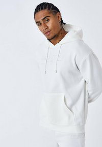 Sudadera blanca con capucha y bolsillo frontal, logo en relieve "PROJECT X", cordones y puños de canalé. Tejido suave con una textura lisa.