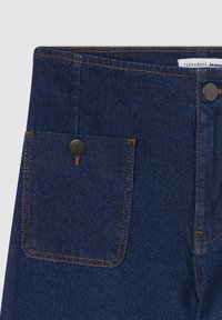 Jeans in denim blu scuro con una tasca frontale dotata di un bottone in metallo nero e cuciture gialle a contrasto lungo i bordi. Texture complessivamente ordinata.