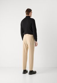 Juodas ilgomis rankovėmis viršus, smėlio spalvos pritaikyti kelniai ir juodi slip-on bateliai. Lygus audinys, prigludusi siluetas, minimalistinis dizainas.