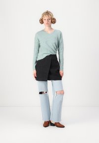 Suéter canelado verde claro, saia preta envolvente, jeans azul claro desgastados e botas de salto castanhas. Um par de auriculares de estampado animal completa o visual.