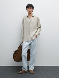 Light beige button-up shirt with a relaxed fit, paired with pale blue trousers, brown suede slip-ons, and a brown suede bag.