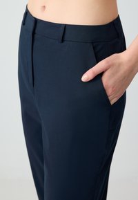 Marineblauwe op maat gemaakte broek met een gladde textuur, voorzien van zijzakken en een aangesloten taille, getoond van de taille tot de bovenbenen.