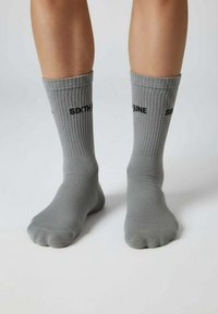 Grijze gebreide sokken met geribbelde textuur. Bovenaan bedrukt met "SIXTH JUNE" in zwarte letters. Enkelhoge uitvoering.