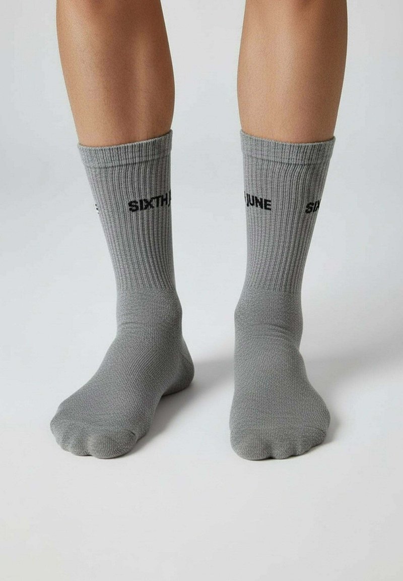 Grijze gebreide sokken met geribbelde textuur. Bovenaan bedrukt met "SIXTH JUNE" in zwarte letters. Enkelhoge uitvoering.