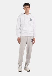 Hvid zip-hoodie med forlommer og grå sweatpants med logo-patch. Tekstureret bomuldsstof, afslappet pasform og ribbede manchetter.
