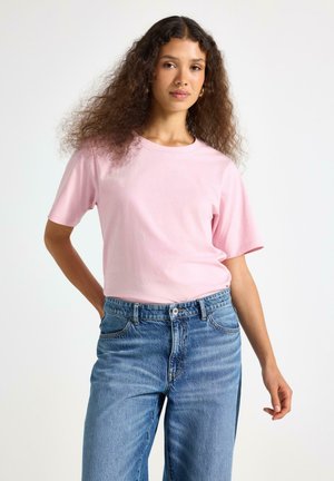 Lyserød bomulds-t-shirt med rund hals og korte ærmer, parret med løstsiddende blå denimjeans. Simpelt design, ingen mønstre.