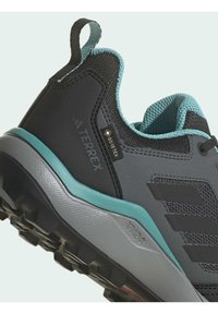 Zapato de senderismo negro y gris con acentos en azul pálido, que presenta una parte superior texturizada, etiqueta GORE-TEX y una suela resistente para tracción.
