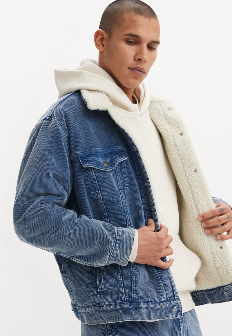 Denim jacket in light blue with a textured corduroy design. Features a white faux shearling collar and interior lining, and snap buttons.