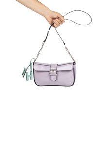 Borsa a tracolla in pelle lilla con forma strutturata, tracolla in catena argentata, profili neri e un charm decorativo verde attaccato.