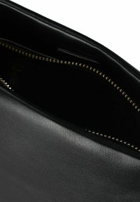 Interno di una borsa nera in pelle con chiusura a zip. Presenta una texture liscia e dettagli zip in tono oro lungo l'apertura.