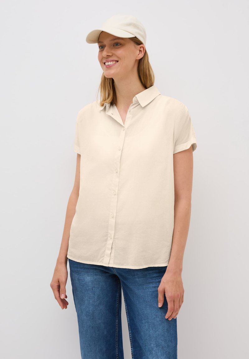 Beige overhemd met korte mouwen, voorzien van een knoopsluiting aan de voorkant en een kraag, gecombineerd met blauwe jeans, met een soepele textuur en een relaxte pasvorm.