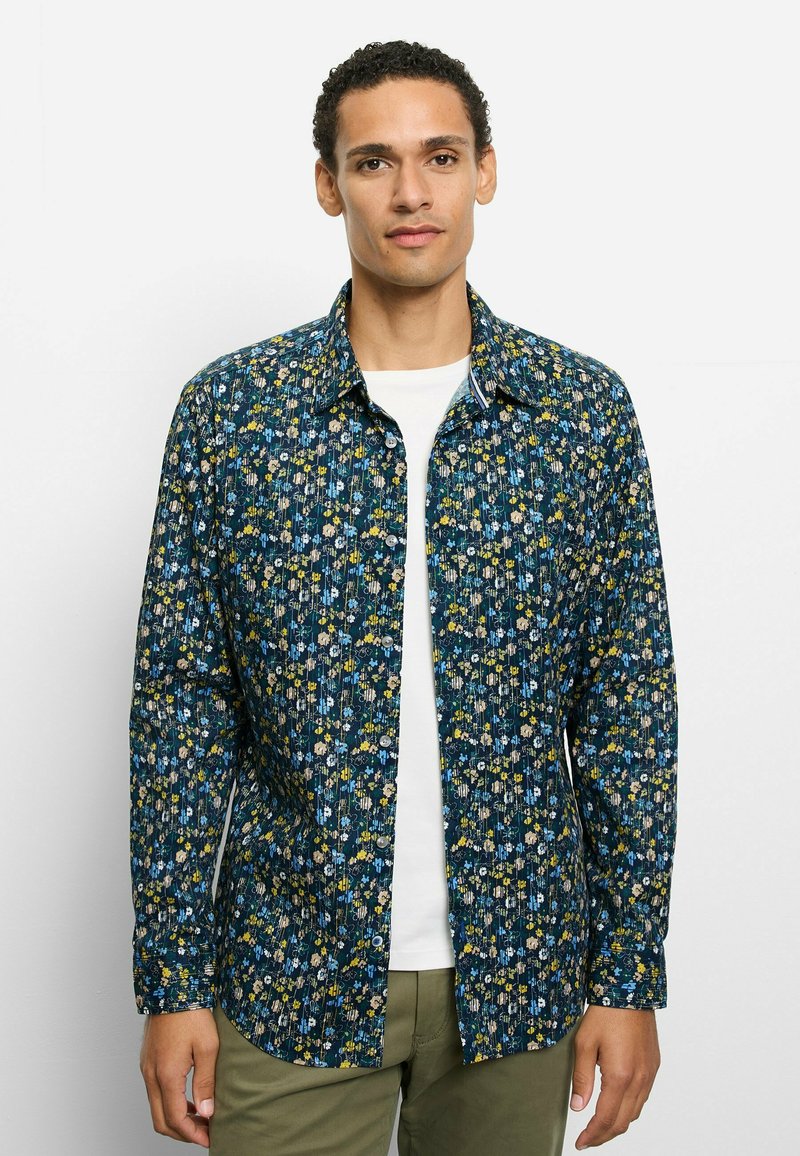 Blau gemustertes Hemd mit kleinen bunten Blumen. Lange Ärmel, Hemdkragen mit Knöpfen und gerader Saum. Weißes Unterhemd sichtbar.