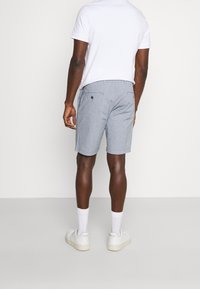 Szare szorty w wzory z gładkim pasem, dwoma tylnymi kieszeniami i luźnym krojem, zestawione z białą koszulką polo oraz białymi trampkami.