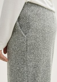Los pantalones de tela en espiga gris presentan una superficie texturada, bolsillos laterales y una cinturilla suave con un cierre de cremallera oculta.