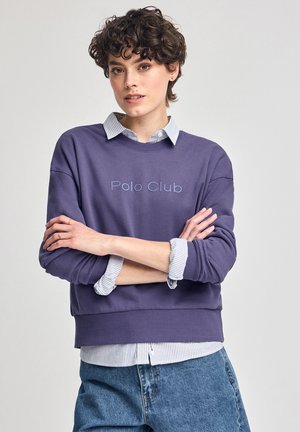 Felpa viola con "Polo Club" ricamato in azzurro chiaro. Indossata sopra una camicia a righe bianche e blu con colletto. Design casual con vestibilità comoda.
