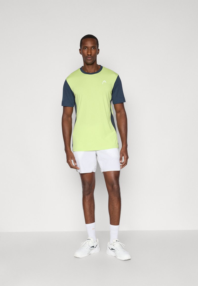 Camiseta deportiva en verde claro y azul marino, con mangas cortas y cuello redondo. El material parece suave, diseño ajustado con un logo en el pecho.