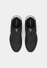 Black athletic shoes with smooth fabric upper, white accents on the collar, and textured rubber soles. Features lace-up design and logo detail.