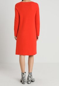 Rotes Strickkleid mit langen Ärmeln, knielanger Schnitt und rundem Ausschnitt, kombiniert mit schwarz-weißen Schlangenprint-Stiefeletten.