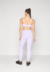 Light purple sports bra and leggings, form-fitting design, smooth texture, adjustable straps, paired with dark athletic shoes.