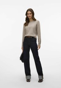 Beige knit sweater, dark denim jeans, brown belt, cuffed hem, black handbag, and brown heeled boots. Simple and tailored fit.