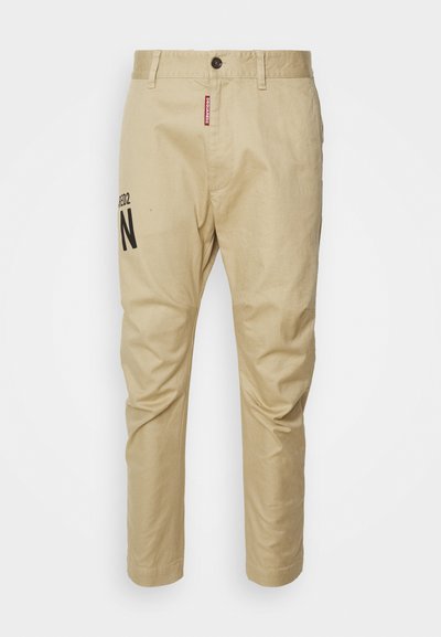 Beige Baumwollhose mit geradem Bein, Frontknopfverschluss und einem bedruckten schwarzen "N"-Logo am linken Bein.