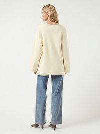 Pull en crème oversize avec un col rond, associé à un jean droit bleu clair et des bottes à talons marron. Texture lisse, design décontracté.