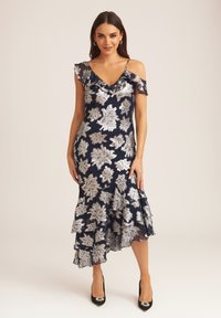 Navy dress with silver floral patterns, ruffled sleeves, a V-neckline, and a layered hem. Paired with black heels featuring embellishments.